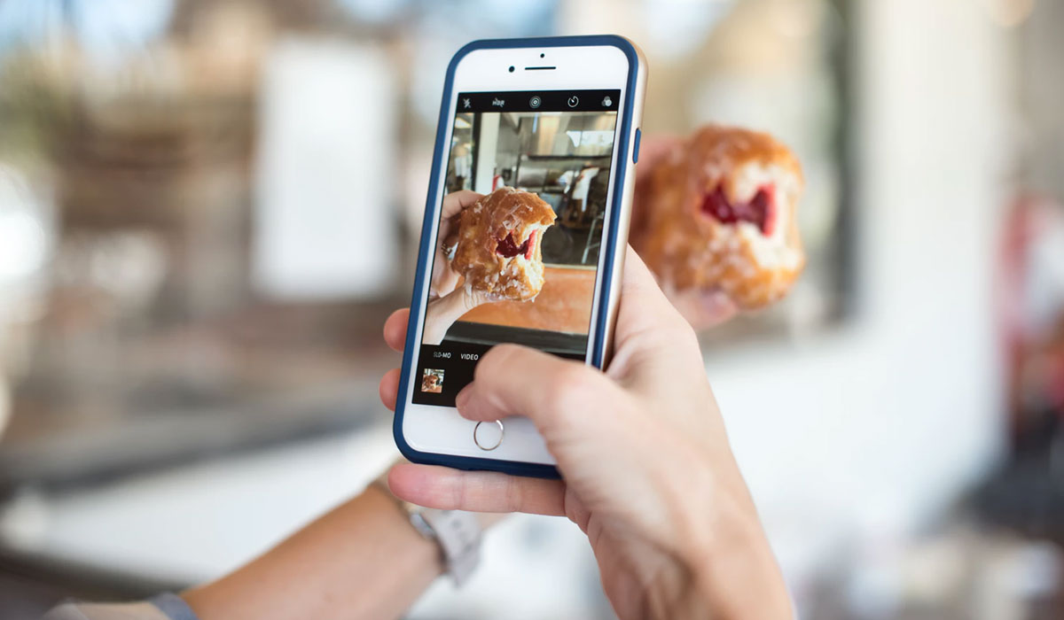 A Person Holds Up A Phone Taking A Picture Of Food