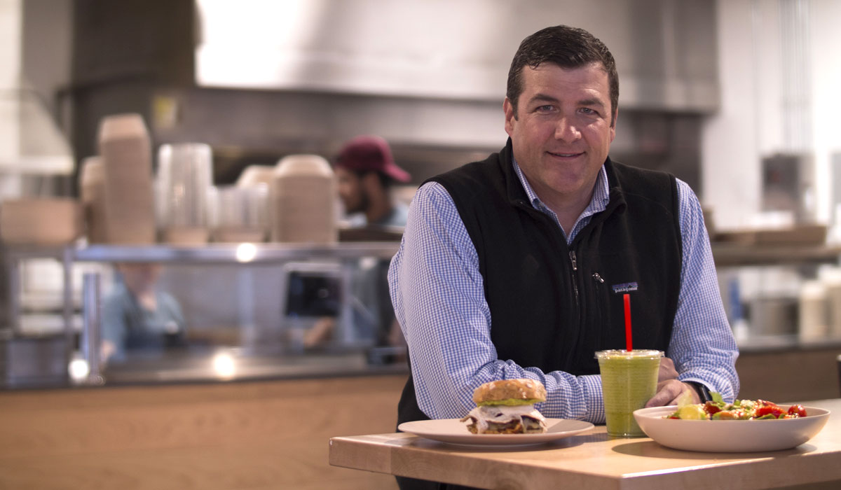 CEO Chris Fuqua Stands At A Table With Food At B.GOOD