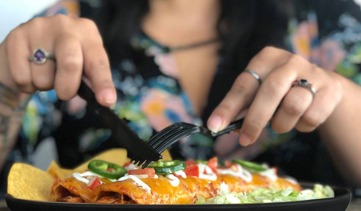 A Customer Cuts A Burrito With A Fork And Knife At Tijuana Flats