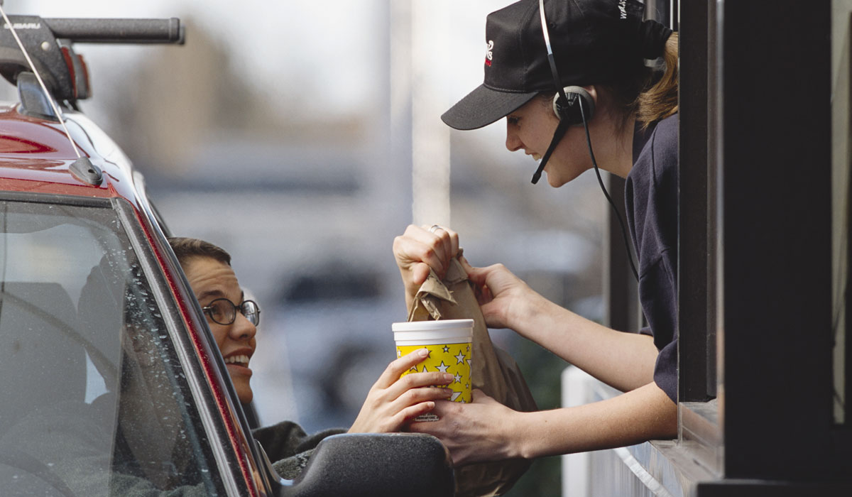 A Restaurant Employee Hands A Customer Food Through A Drive Thru Window