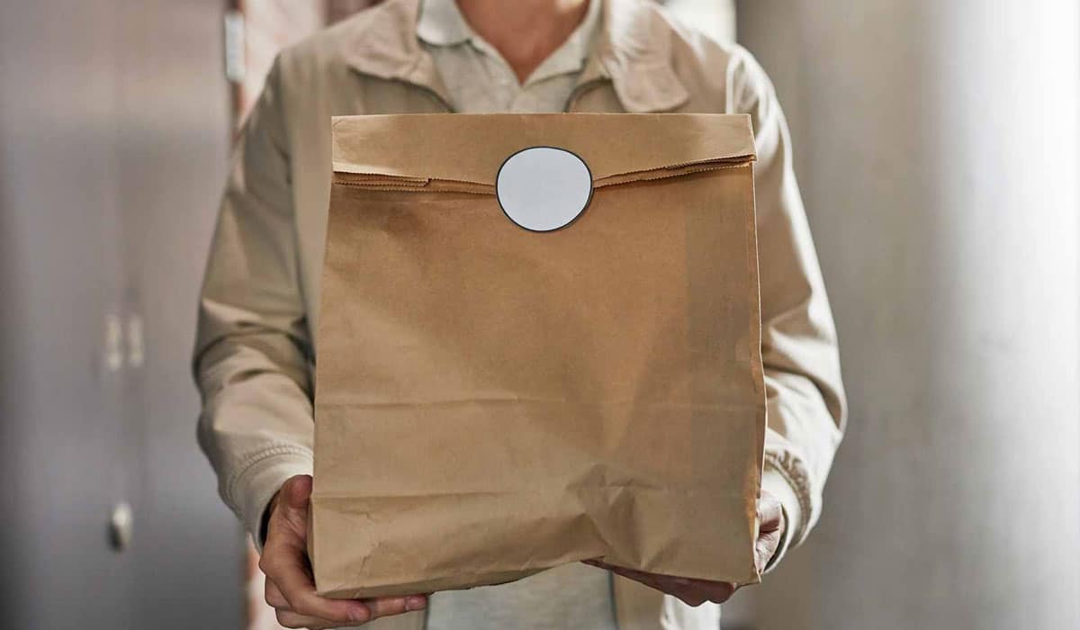 A Restaurant Employee Carrying A Brown Paper Bag Of Food