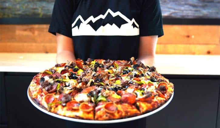 An employee holding a Mountain Mike's pizza.