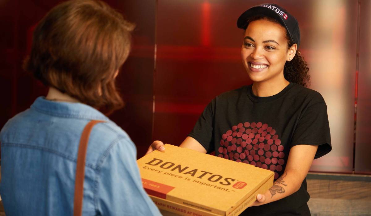 Donatos employee handing over a pizza.