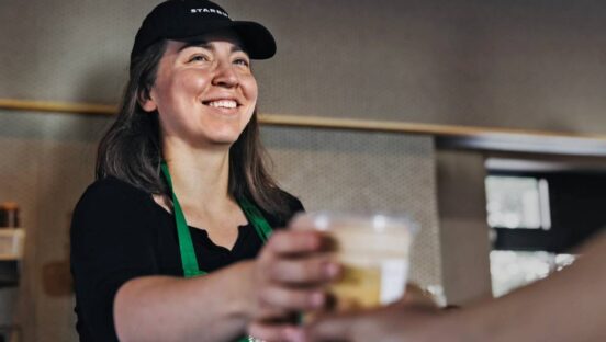 Starbucks employee handing cup of coffee to guest.