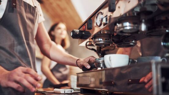 A barista making coffee with a white mug.