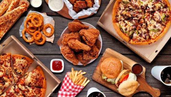 . Pizza, hamburgers, fried chicken and sides. Above view on a dark wood background.