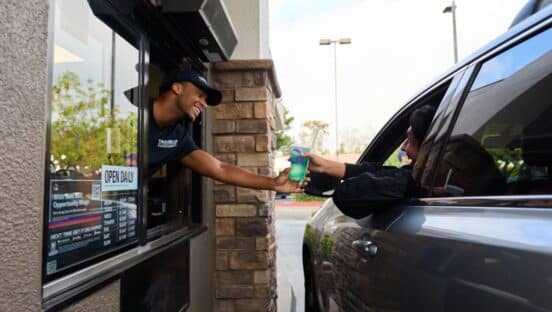 Taco Bell drive-thru employee handing a drink to a customer in a car.