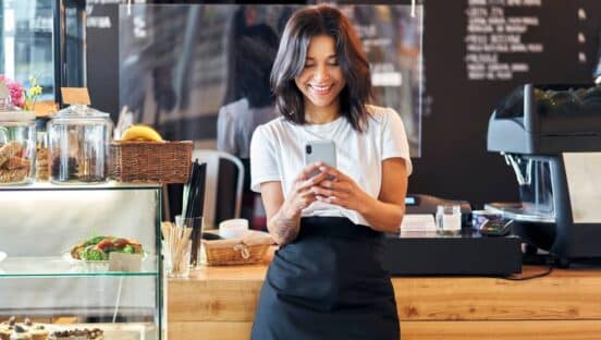 Restaurant employee standing in front of counter looking at phone.